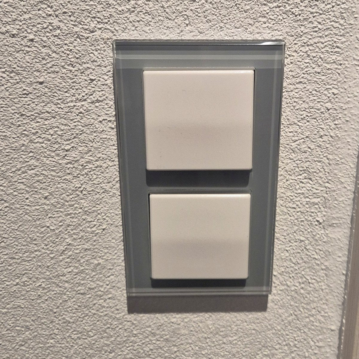 Lichtschalter mit Glasrahmen an einer verputzten Wand